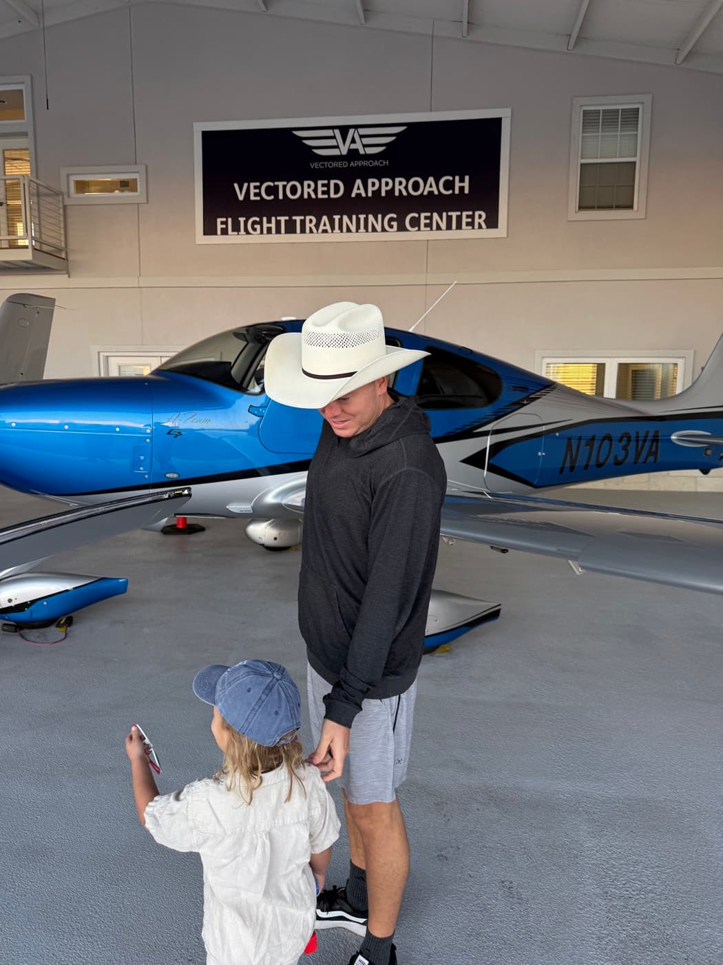 Andy in a cowboy hat with his kid in front of a Cirrus in the hangar